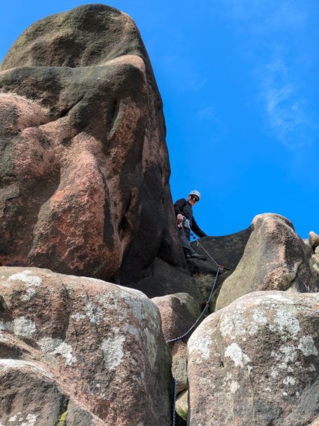 Leading on Ramshaw rocks Climber scaling a rocky formation under a clear blue sky.